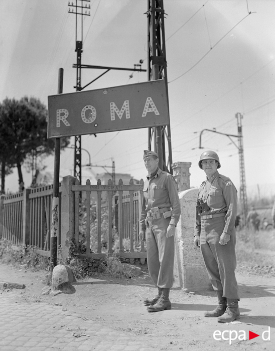 <p class='eng'>Description : Le lieutenant general Mark Wayne Clark, commandant la Ve armée américaine, pose devant un panneau indicateur aux portes de Rome ; à ses côtés, l’un de ses chefs de corps d’armée, le major general Geoffrey Keyes, commandant le 2e corps d’armée. Date : 5 juin 1944<br />Lieu : Rome, Italie Photographe : inconnu<br />Origine: SCA-ECPAD<br />Référence : TERRE-229-5166</p>