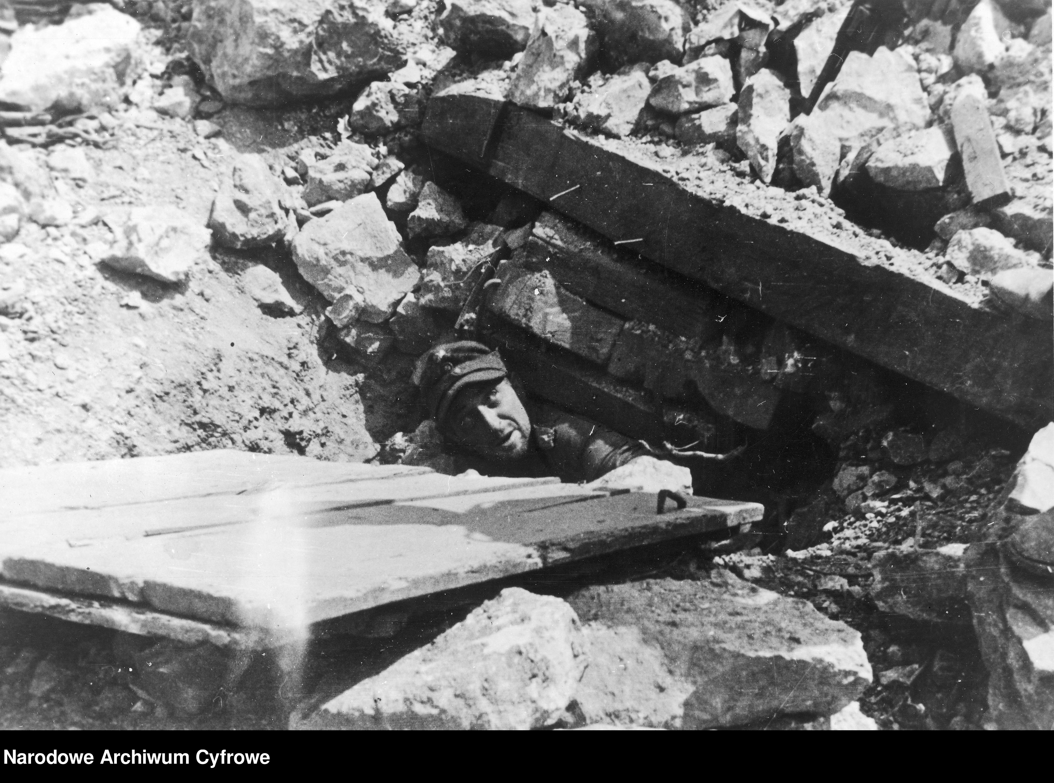 <p>Piedimonte San Germano, maggio 1944.<br />La cattura di tre paracadutisti tedeschi, intrappolati sotto le macerie del paese. Le riprese furono eseguite da un fotoreporter inglese e dal fotoreporter polacco Tadeus Szumanski.</p><p class='eng'>1944/05/25<br />A German soldier comes out of a bunker excavated from the rubble.<br />NAC 3/24/0/-/457/8</p>