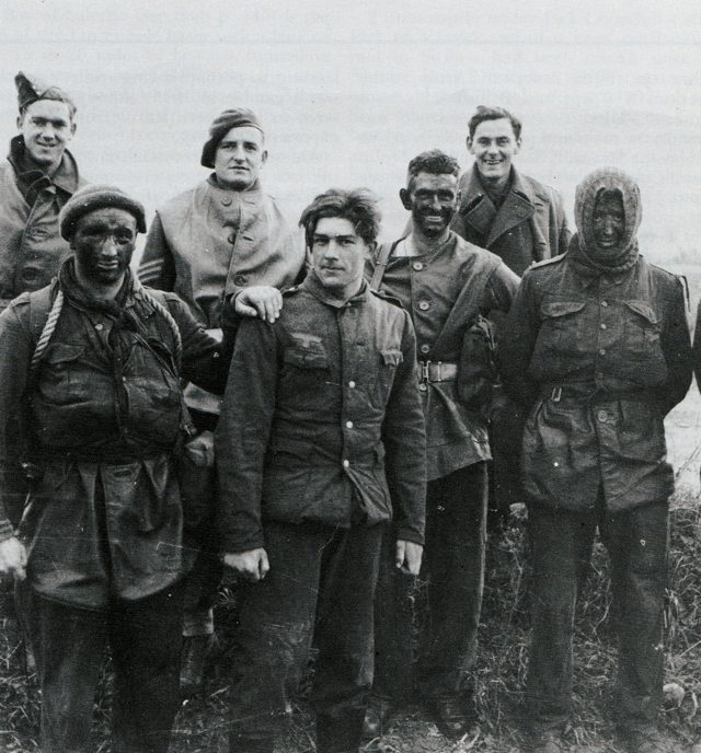 <p>30 dicembre 1943. Alcuni membri del No.9 Commando posano per una fotografia con uno dei soldati tedeschi catturati nel corso del raid (operazione Partridge) nelle posizioni nemiche sul fiume Garigliano.</p><p class='eng'>A Commando raid was carried out by men of the 9 Commando on enemy positions around the River Garigliano, North of Mondragone, on the night 29/30 December, 1943. The Commandos came inshore in assault boats and ducks, and waded inshore up to they necks to water. The enemy was taken completely by surprise as the Commandos closed in with bagpipes playing and guns blazing. Many German prisoners were taken and brought back.<br /><br />A group of Commandos with a 19-year old German prisoner in the centre.<br />Taken by Sgt. Mott. 30.12.43. © IWM NA 10443<br /><br />----<br />from https://www.facebook.com/karen.sleith<br />My Granda Tommy (paddy) Sleith is 1st on the right of photo 3454 with his face dark and wearing a snood . He is also 2nd on the right of photo 3453 again wearing a snood drinking from a cup.<br /><br /></p>
