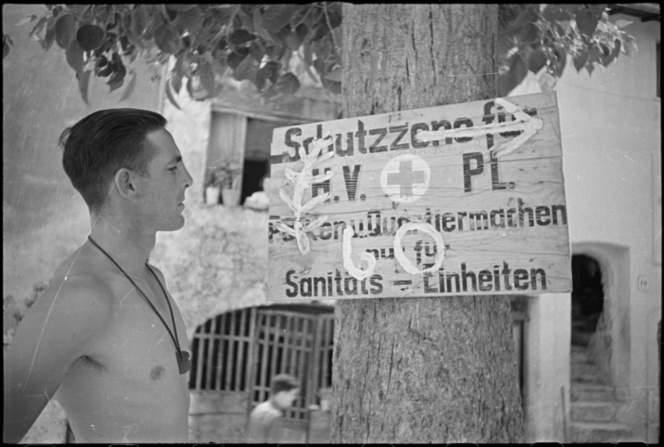<p class='eng'>J T Needham (Hamilton) looks at the New Zealand sign, the Silver Fern, superimposed over this German sign near the 6 NZ Field Ambulance's Advanced Dressing Station at Sora in Italy, during World War II. Photograph taken circa 4 June 1944 by George Frederick Kaye.</p>