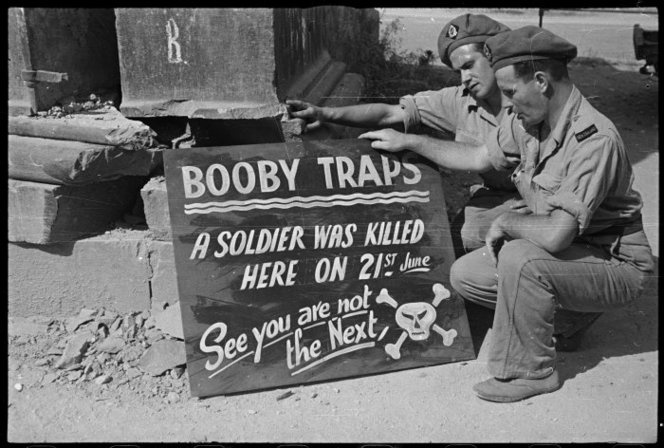 <p class='eng'>Sign warning soldiers about booby traps, erected by NZ Division Engineers on a road near Sora, Italy, during World War II. Shows R G Young and F H Hutson, both from Southland. Photograph taken circa 22 June 1944 by George Kaye.</p>